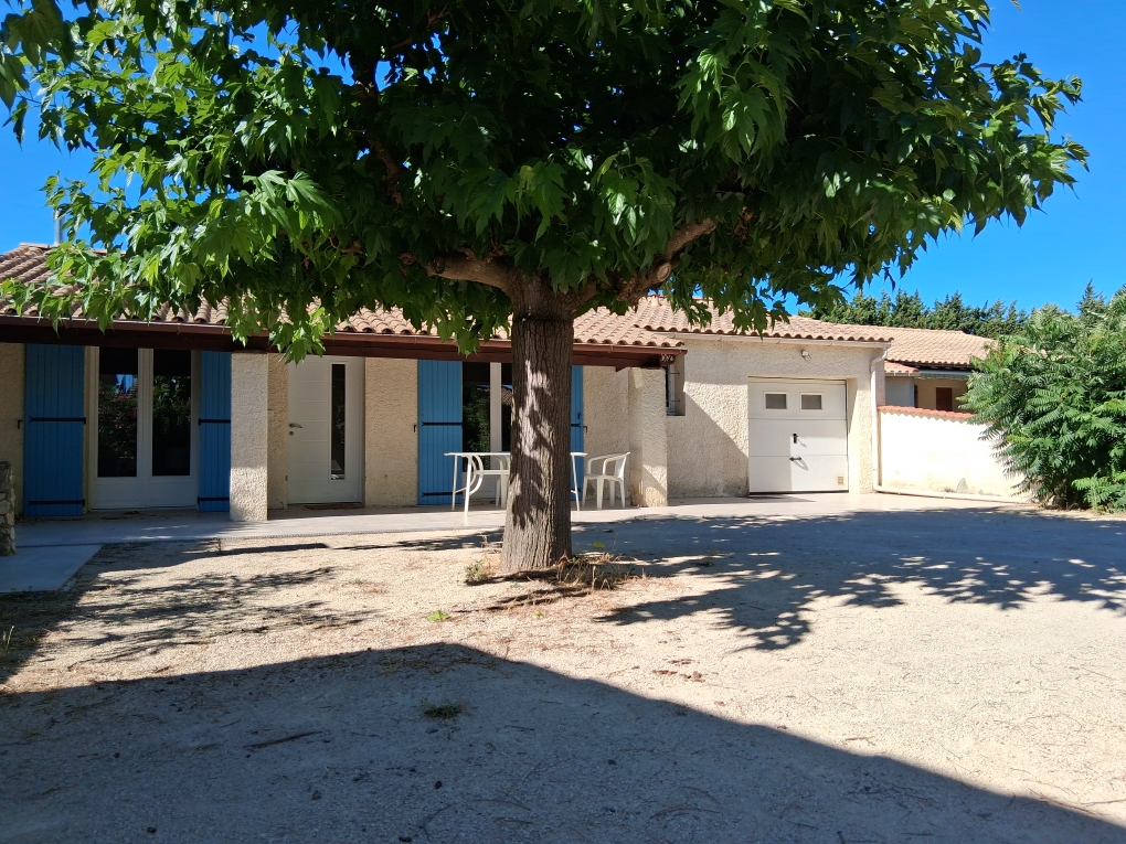 Ein einstöckiges provenzalisches Haus mit blauen Fensterläden und einer weißen Garage unter einem großen Laubbaum mit Aussicht