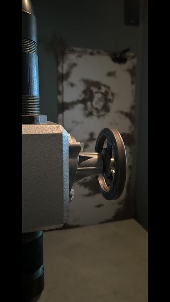 Eine Nahaufnahme eines Metallventilrads in einer industriellen Umgebung mit einer rostigen, strukturierten Tür im Hintergrund.