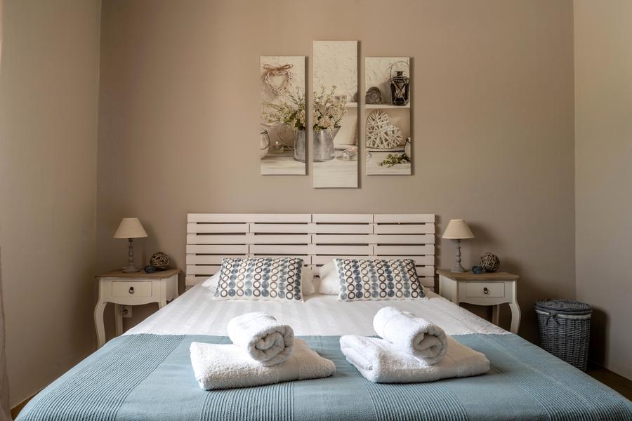 Beiges Schlafzimmer, himmelblaue Bettdecke, Triptychon an der Wand und 2 weiße Nachttische aus Holz