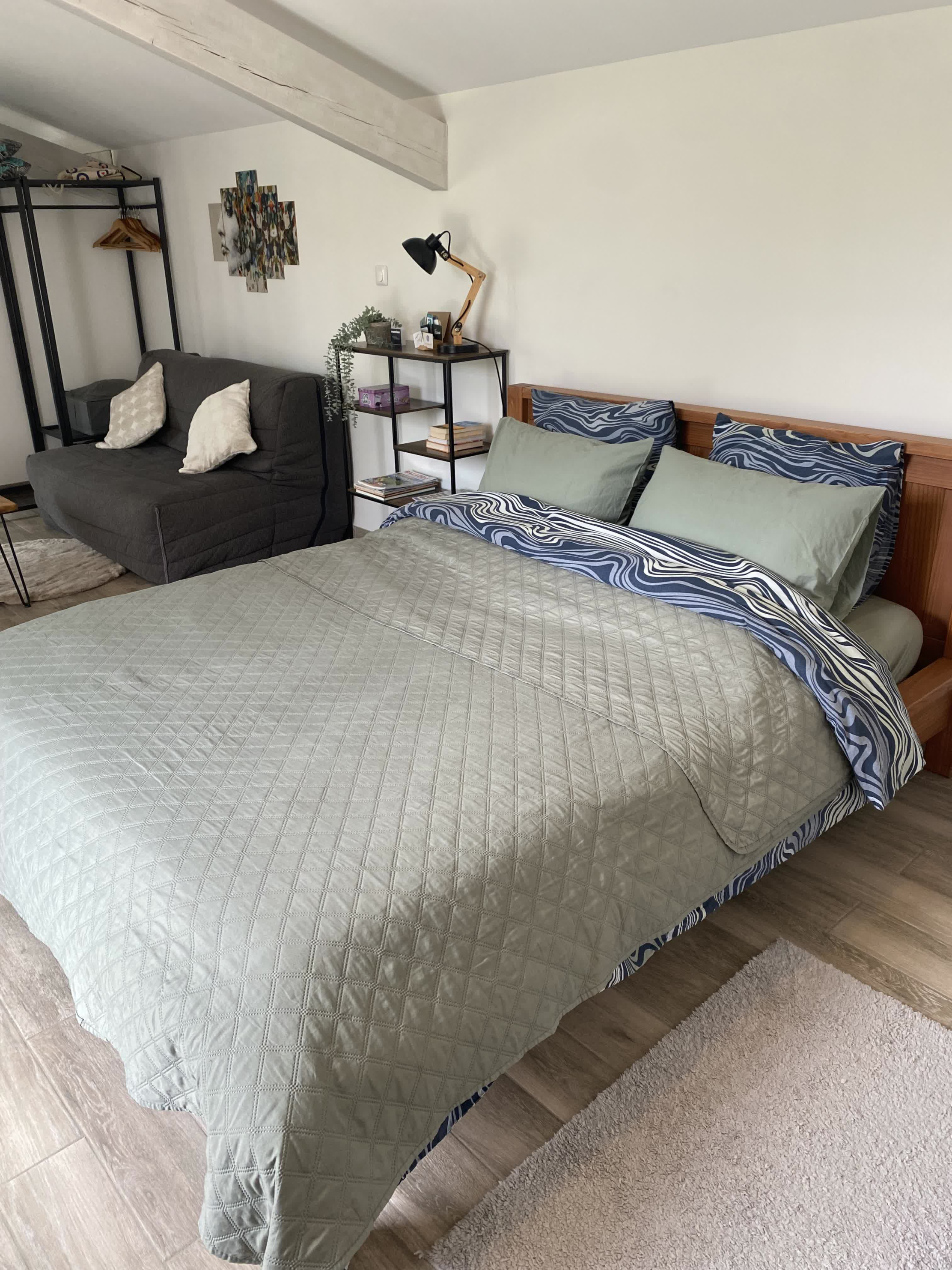 Ruhiges und raffiniertes Zimmer mit einem großen Doppelbett aus grüner Bettwäsche, einem grauen Sofa und modernem Dekor.