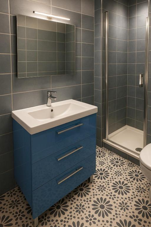 Modernes Badezimmer mit Dusche, blauem Waschtisch und grafischen Fliesen auf dem Boden. Ein renovierter Raum, der modernen Komfort und sorgfältige dekorative Details vereint.