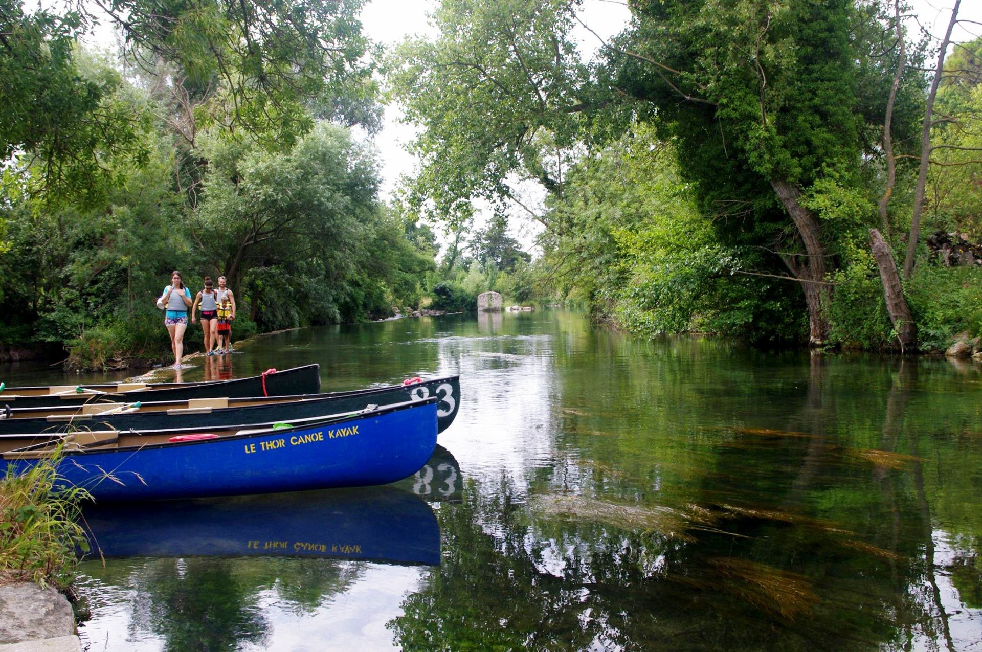 Kanus des Thor Canoe Kayak Club, die auf dem kristallklaren Wasser der Sorgue festgemacht sind, in einer ruhigen und grünen Umgebung, die der Entspannung und natürlichen Freizeitgestaltung förderlich ist.