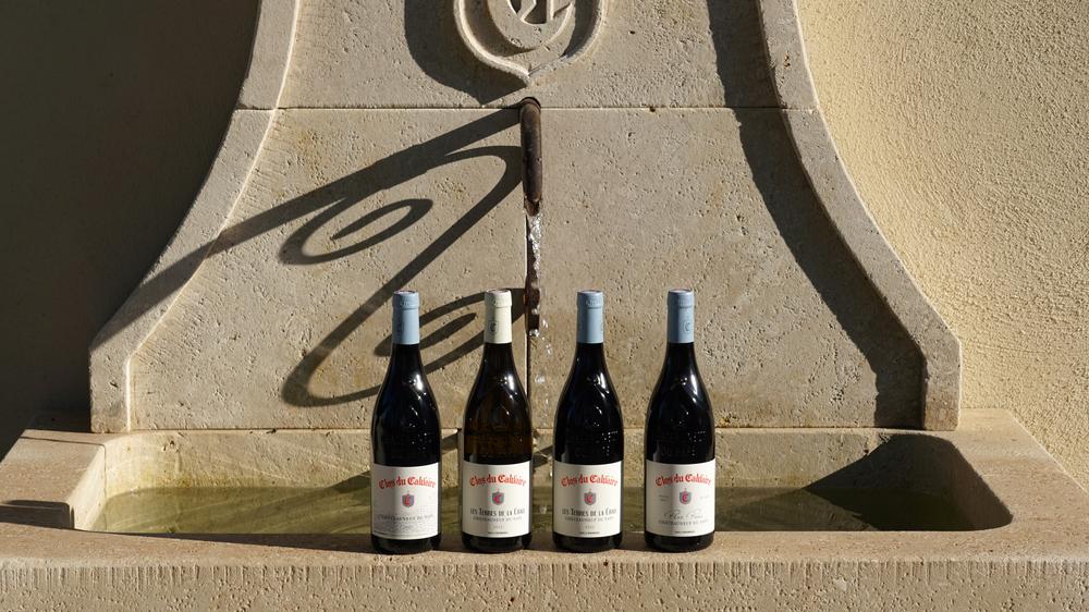 Eine Auswahl an Flaschen von Clos du Calvaire, präsentiert vor einem provenzalischen Steinbrunnen. Diese Inszenierung veranschaulicht die verschiedenen Cuvées, die das Weingut im Herzen von