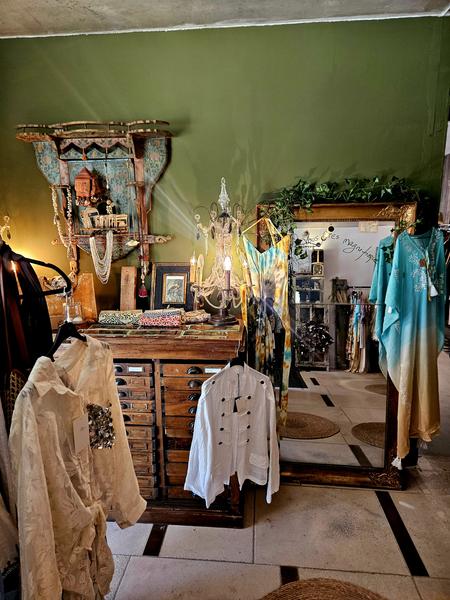 Dieser Raum bietet verschiedene Kleidungsstücke mit böhmischen Inspirationen: leichte Hemden, fließende Stücke und farbenfrohe Outfits. Die antiken Möbel, der vergoldete Spiegel und die Dekorationsgegenstände bilden ein einzigartiges Dekor, das sowohl elegant als auch vielseitig ist.