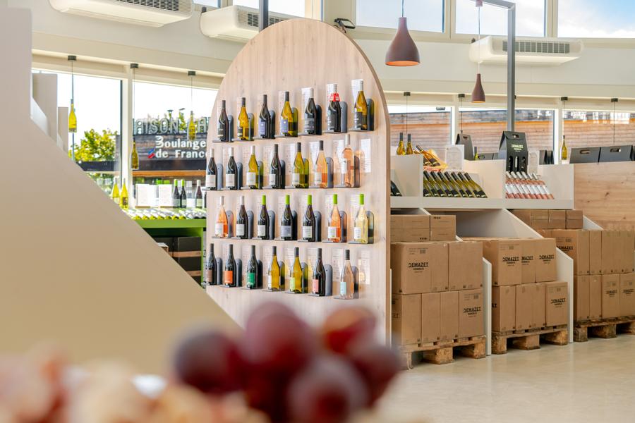 Innenansicht des Demazet-Kellers, hell und modern, mit einer großen Auswahl an Weinflaschen, präsentiert auf Holzregalen. Der Raum hebt die verschiedenen Weine des Kellers in einer modernen und einladenden Atmosphäre hervor.