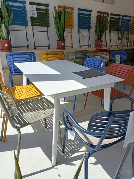 Ein Ausstellungsraum präsentiert Gartentische und Stühle in verschiedenen Farbtönen, von Blau über Gelb bis Grün und Rot. Pflanzen runden diese Inszenierung ab, die der Gestaltung der Terrasse und des Außenbereichs gewidmet ist.